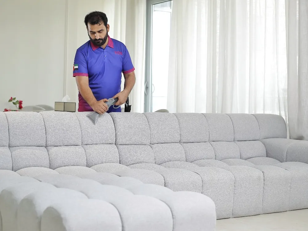 A TopOne cleaner steam cleaning a grey fabric sofa in a Dubai home